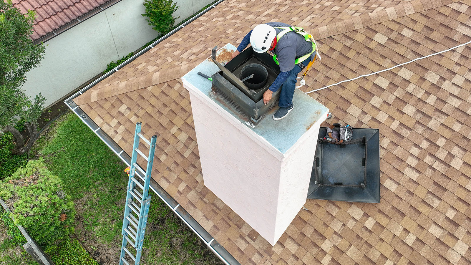 Chimney technicians on the roof performing installation wearing harnesses and helmets.