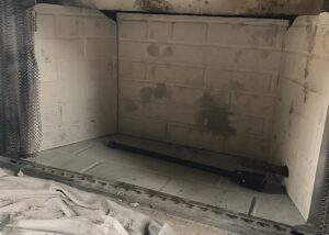 Interior of a wood-burning firebox with refractory panels, soot staining and a chimney sweep rod resting on a drop cloth